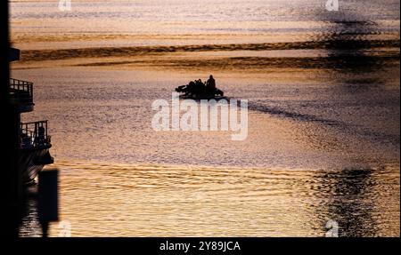 Silhuette von Menschen, die das Boot im Victoria Harbour in der Abenddämmerung rudern, mit hübscher Farbe des Sonnenuntergangs, die auf der Wasseroberfläche in Melbourne, Victoria, Australien, abfällt Stockfoto