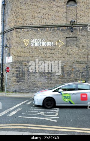 Verschwommenes Taxi an einer Kreuzung mit einem Schild, das zum Guinness Storehouse am St. James Gate, Dublin, Irland zeigt; Touristenattraktion. Stockfoto