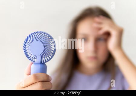 Mädchen mit einem tragbaren Ventilator, der sich während der Sommerhitze ins Gesicht bläst Stockfoto