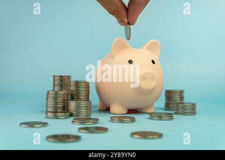 Niedliche Schweinebank, rosa Farbe mit Münzstapeln auf blauem Hintergrund mit Hand Münze. Geld sparen, Investitions- und Finanzierungskonzept. Stockfoto