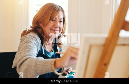 Lächeln, Seniorin und Malerei auf Leinwand für kreative Kunst, Talent und Inspiration. Malerpalette, Künstler und Pinsel für Ruhestand, Heim Stockfoto