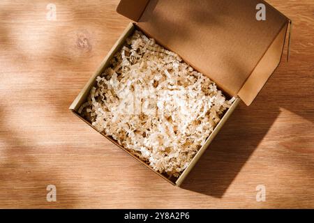 Öffnen Sie den Karton mit geschredderter Papierfüllung auf einem Holztisch Stockfoto