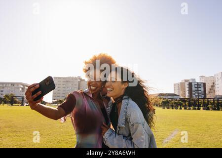 Zwei beste Freunde an der Universität, die einen sonnigen Tag im Freien genießen, lächeln und gemeinsam ein Selfie in einem Stadtpark machen. Stockfoto