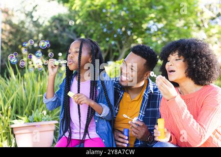 Glücklicher afroamerikanischer Vater, Mutter und Tochter blasen Blasen in sonnigem Garten, Kopierraum Stockfoto