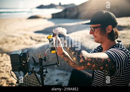 Videofilmer, Mann und Videokamera am Strand für Filmproduktion, Fotografie oder Naturdokumentation. Kameramann, Aufnahme und Aufnahme hinter dem Stockfoto