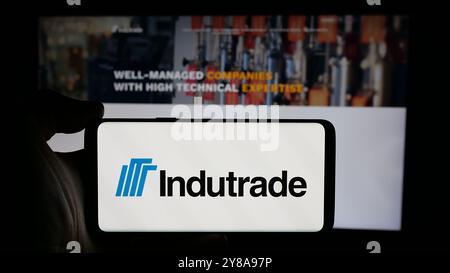 Person, die ein Mobiltelefon mit dem Logo des schwedischen Industrieunternehmens Indutrade ab auf dem Bildschirm vor der Webseite hält. Schwerpunkt auf dem Display des Telefons. Stockfoto