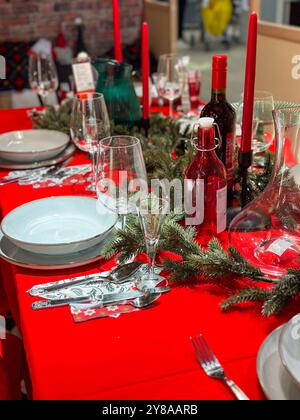 Der festliche Weihnachtstisch ist mit festlichen Dekorationen geschmückt und bereit für ein fröhliches Treffen im Winter. Leuchtend rote Tischdecke und elegantes Geschirr Stockfoto