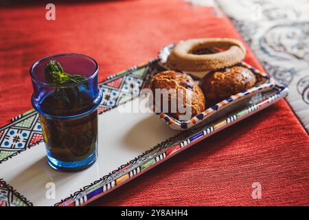 Traditioneller marokkanischer Pfefferminztee und marokkanische Kekse auf einer traditionellen berbere-Platte auf einem roten, traditionellen marokkanischen Teppich Stockfoto