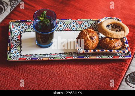 Traditioneller marokkanischer Pfefferminztee und marokkanische Kekse auf einer traditionellen berbere-Platte auf einem roten, traditionellen marokkanischen Teppich Stockfoto