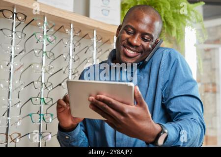Lächelnder Optometrist Geschäftsinhaber hält Tablet mit Brillendisplay im Hintergrund Stockfoto