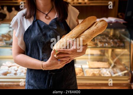 Junger Bäcker, der frische Brotlaibe in gemütlicher Bäckerei hält Stockfoto