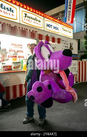 Ein Mann, der einen riesigen lila Plüschtier-Hund hält Stockfoto