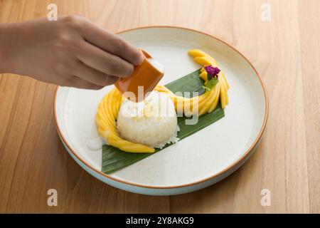 Vor dem Genuss von Mango-Klebereis ist es wichtig, ihn mit Kokosmilch zu beträufeln, um einen leichten Salzgehalt hinzuzufügen, der die Süße des r Stockfoto