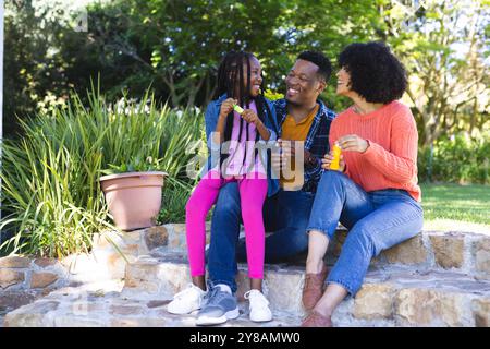 Glücklicher afroamerikanischer Vater, Mutter und Tochter blasen Blasen in sonnigem Garten, Kopierraum Stockfoto