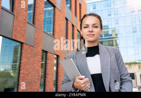 Selbstbewusste Geschäftsfrau mit Tablet vor einem modernen Bürogebäude. Stockfoto