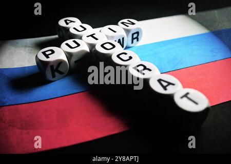 Buchstabenwürfel bilden die Wörter Putin und Autocrat in Kreuzform auf russischer Flagge, Buchstabenwürfel formen die Wörter Putin und Autocrat (engl.) In Kreuzf Stockfoto