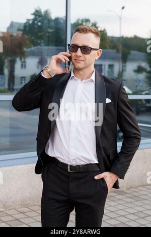 Eleganter Geschäftsmann im stilvollen schwarzen Anzug, der sich an einem Telefongespräch beteiligt. Stockfoto
