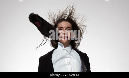 Schwarzer Lederschuh schlägt vor weißem Studiohintergrund in die Wange der Frau. Frau im Geschäft. Geschlechterrollen. Stockfoto