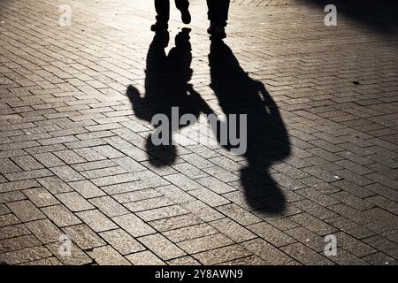Silhouetten von zwei Leuten, die die Straße entlang laufen. Schatten von Erwachsenen und Kindern auf dem Gehweg Stockfoto
