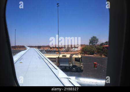 Blick auf den Flugzeugflügel des Tankwagens auf dem Vorfeld und Uluru vom Ayers Rock Airport (Connellan Airport) in Yulara, Uluru, Zentralaustralien Stockfoto