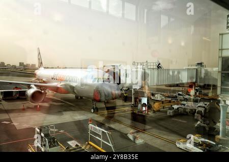 Sydney Airport, Reflektionen und ein Jetstar-Flugzeug, das auf dem Vorfeld einer Jetbrücke vom Terminal aus geparkt ist Stockfoto