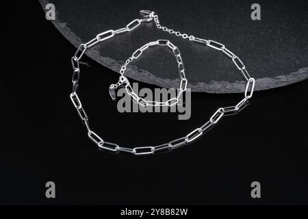 Zwei Ketten hängen an einer Keramikschale. Metallkette und Armband auf schwarzem Hintergrund Nahaufnahme. Minimalistische Schmuckketten aus Silber. Stockfoto