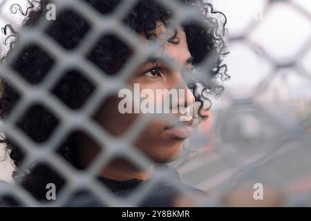 teenager mit lockigem Haar hinter Metallzaun Stockfoto