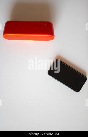 Roter kabelloser Lautsprecher und schwarzes Mobiltelefon auf einem weißen Tisch Stockfoto