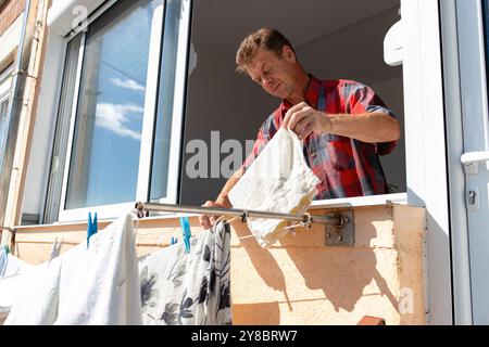 Ein reifer Mann zieht seine Wäsche durch das Terrassenfenster aus. Stockfoto