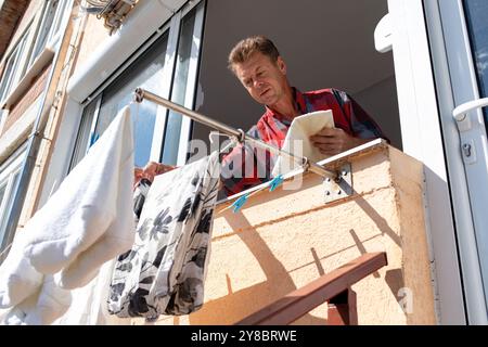 Ein reifer Mann zieht seine Wäsche durch das Terrassenfenster aus. Stockfoto