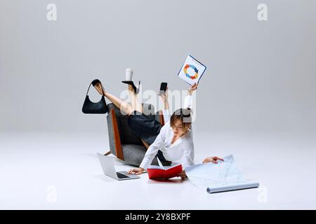 Geschäftsfrau in der Mitte der Aufgabe, Balance zwischen Zwischenablage, Telefon und Kaffeetasse, während sie auf dem Boden Papier liest. Effizienz unter Druck. Stockfoto