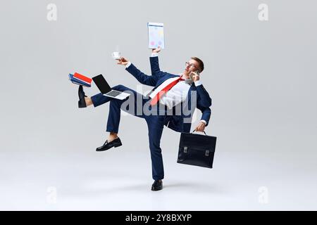 Geschäftsmann-Multitasking, Balancierung mit Kaffeetasse, Laptop und Telefon in dynamischer Haltung, zeigt Kunst, alles zu erledigen. Stockfoto