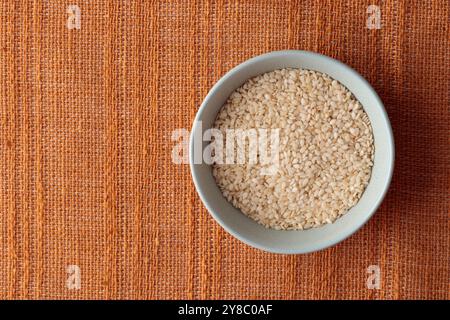 Nahaufnahme von organischen weißen Sesamsamen, Sesamum indicum in einer Keramikschale mit braunem Hintergrund, Zutat o Kimchi. Draufsicht Stockfoto