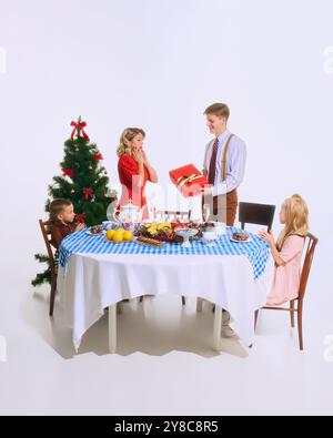 Die Familie genießt ein Überraschungsgeschenk während ihrer Weihnachtsmahlzeit. Feiertagstisch voller festlicher Leckereien, die eine fröhliche Feier schaffen. Stockfoto