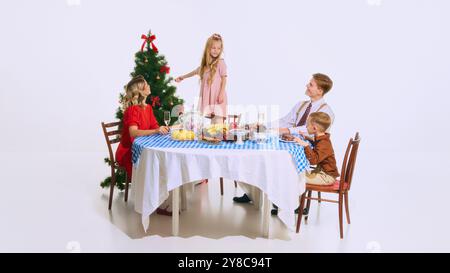 Das kleine Mädchen schmückt den Weihnachtsbaum, während die Familie ihr Essen genießt. Sie verleiht der festlichen Szene eine süße Note, voller Wärme und Feiertagsstimmung Stockfoto