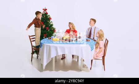 Junge steht auf Stuhl und singt neben dem Weihnachtsbaum, während seine Familie zusieht und lächelt. Weihnachtsstimmung in vollem Gange mit Dekoration und festlichem Ambiente Stockfoto