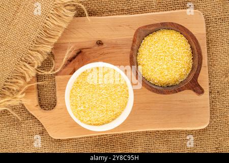 Ungekochte Maiskörner in Keramik- und Holzgerichten auf Jute-Tuch, Makro, Blick von oben. Stockfoto