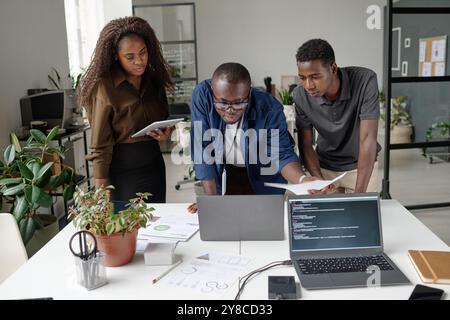 Afroamerikanisches Team junger und erfolgreicher Entwickler diskutiert und erstellt neue Codes in White Office Stockfoto