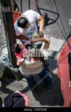 Mexiko-Stadt CDMX 2009: Armes mexikanisches Familienessen; Mutter schenkt dem Kind Coca-Cola und Ehemann isst Tacos an der Stadtecke Stockfoto