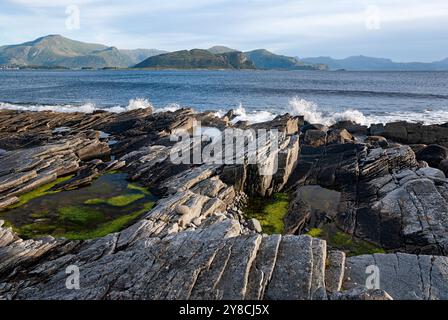 Sanfte Wellen krachen gegen zerklüftete Felsen und enthüllen lebendige Gezeitenbecken und atemberaubende Berge unter einem weichen Morgenhimmel. Stockfoto