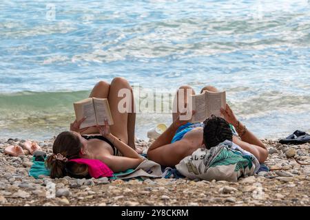 Paare liegen auf Handtüchern und sonnen sich an einem mittelmeerstrand und lesen Bücher in der warmen Sommersonne in Griechenland Stockfoto