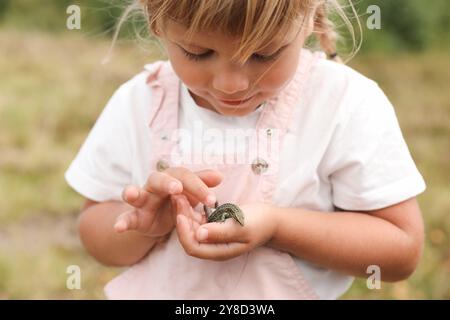 Kleines Mädchen, das eine Eidechse auf verschwommenem Hintergrund hält. Kind genießt wunderschöne Natur Stockfoto