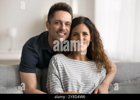 Ein schöner, liebevoller Ehemann umarmt eine hübsche Frau, die auf der Couch sitzt Stockfoto
