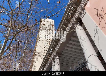 Flacher Blick auf das alte renovierte Haus und das moderne hohe Gebäude dahinter, eingerahmt von Bäumen ohne Blätter. Horizontale, diagonale und vertikale Linien Stockfoto