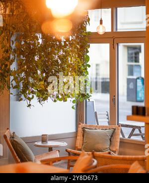 Gemütliche Café-Ecke mit Rattanstuhl, kleinem runden Tisch mit Kaffee, Gebäck und einer Vase mit getrockneten Blumen, umgeben von üppigen hängenden Pflanzen Stockfoto