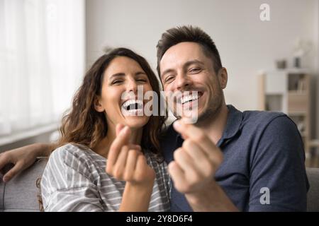 Fröhliches glückliches Paar, das in die Kamera schaut, lacht, Fingerherz zeigt Stockfoto