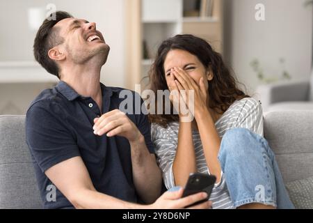 Fröhliches Millennial-Paar, das Smartphone auf dem Heimsofa hält Stockfoto