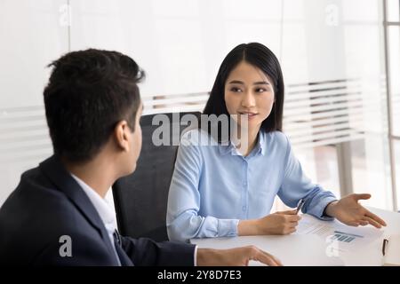Positive junge asiatische Geschäftsfrau, die beim Treffen mit einem männlichen Kollegen spricht Stockfoto