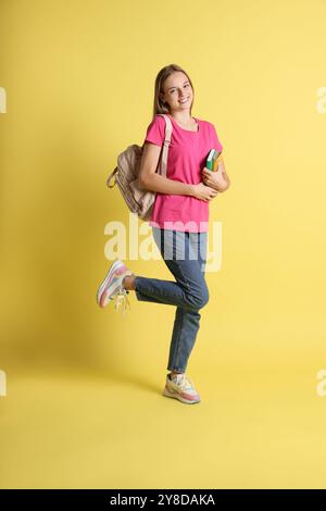 Teenager-Mädchen mit Büchern und Rucksack auf gelbem Hintergrund Stockfoto