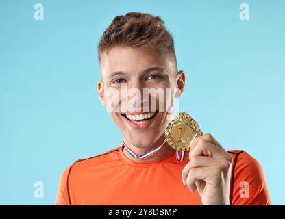 Glücklicher Gewinner mit goldener Medaille auf hellblauem Hintergrund Stockfoto